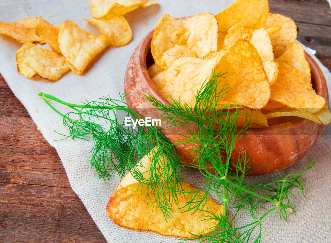 Crispy potato chips with dill in a wooden bowl on linen napkin