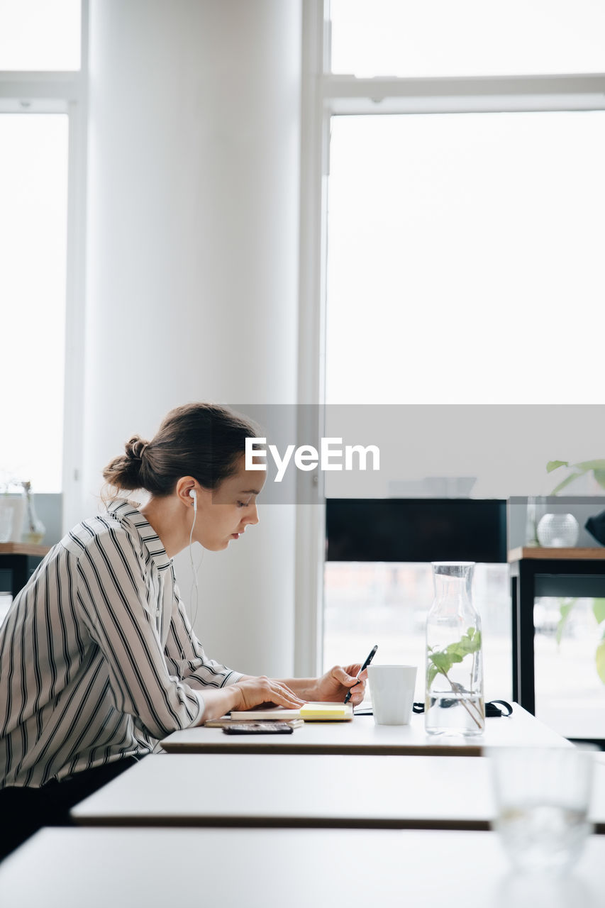 Side view of businesswoman listening music while working at desk in office