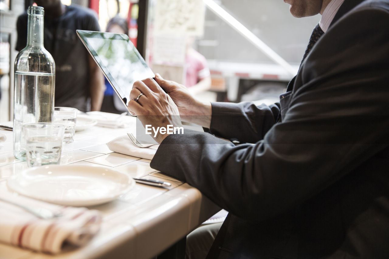 Side view of businessman using tablet computer while sitting at table in restaurant
