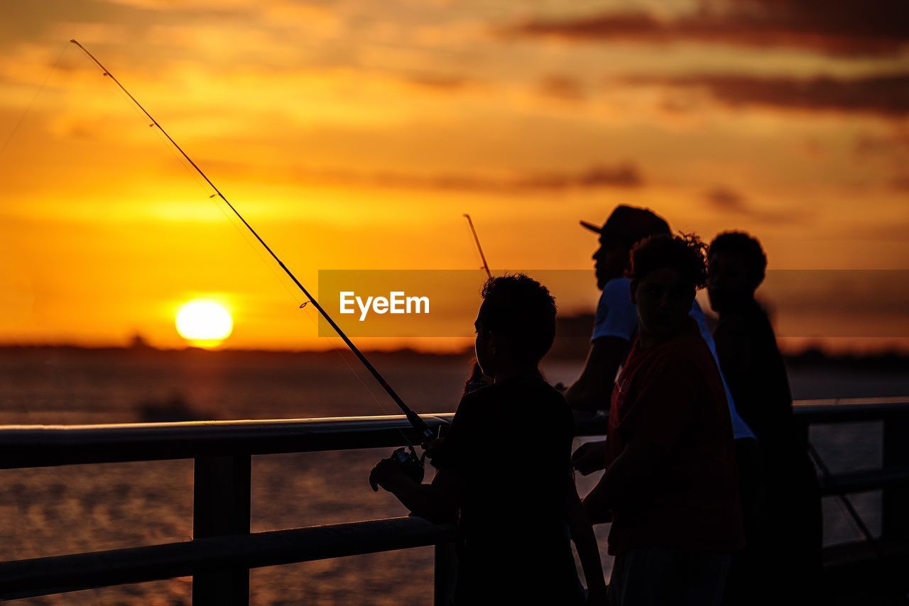 Silhouette of people standing by sea against sky during sunset