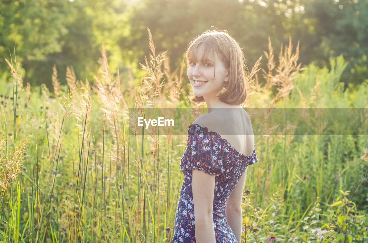 Portrait of smiling young woman standing at field