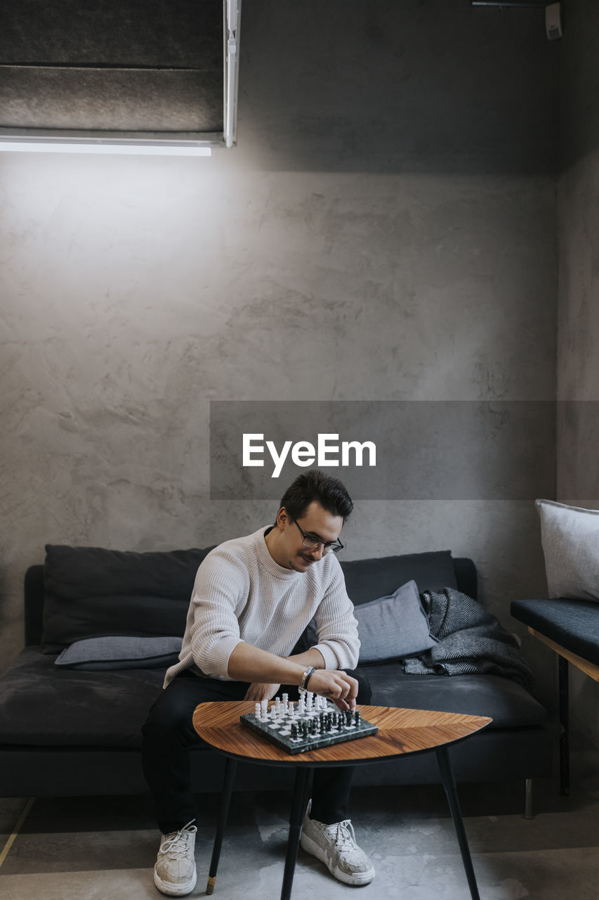 Young male entrepreneur playing chess while sitting on sofa at workplace