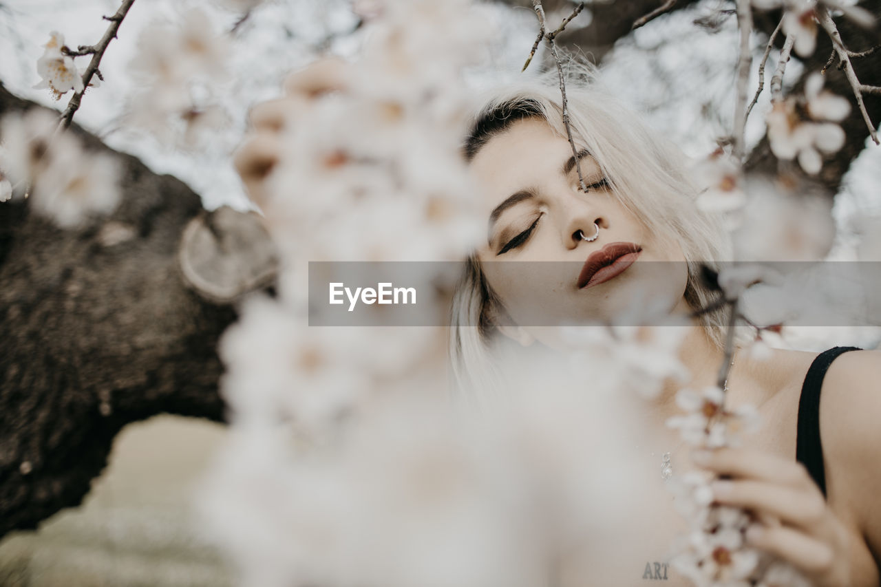 Young woman with eyes closed standing under blossoming almond tree