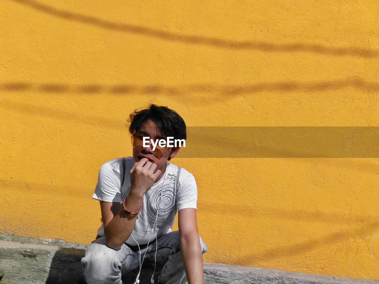 FULL LENGTH OF YOUNG MAN SITTING AGAINST YELLOW WALL