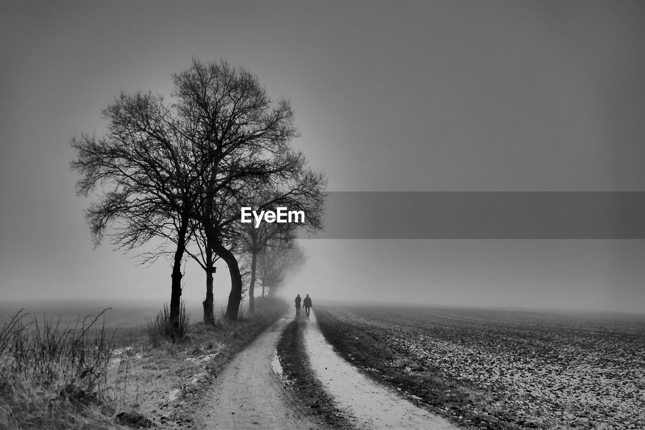 A couple walking through the fields on a foggy  and rainy  day  in november. 