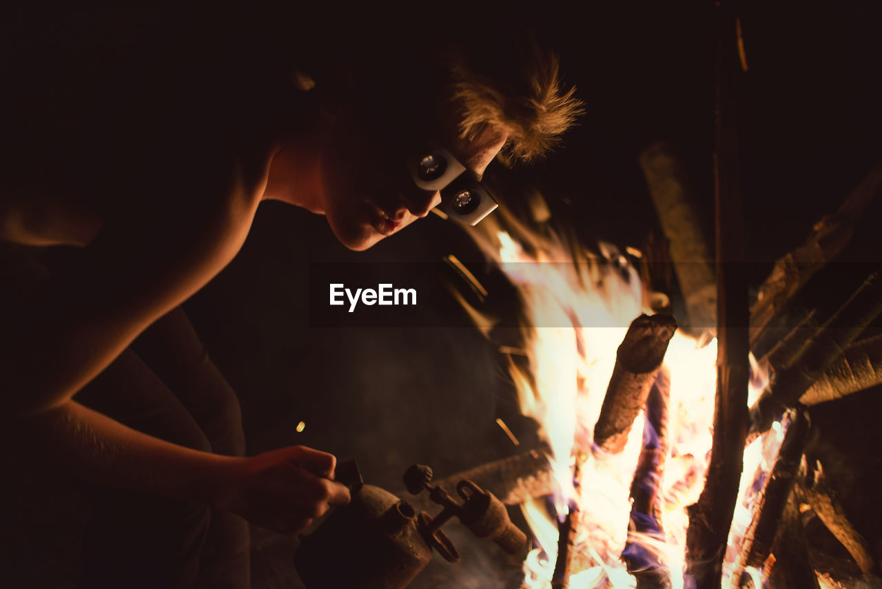 Man in protective eyewear holding equipment by bonfire at night