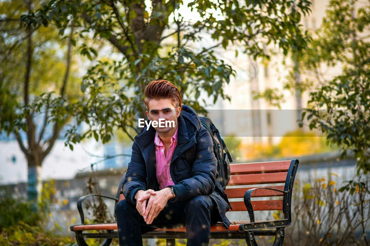 Side view of young man sitting on bench in park