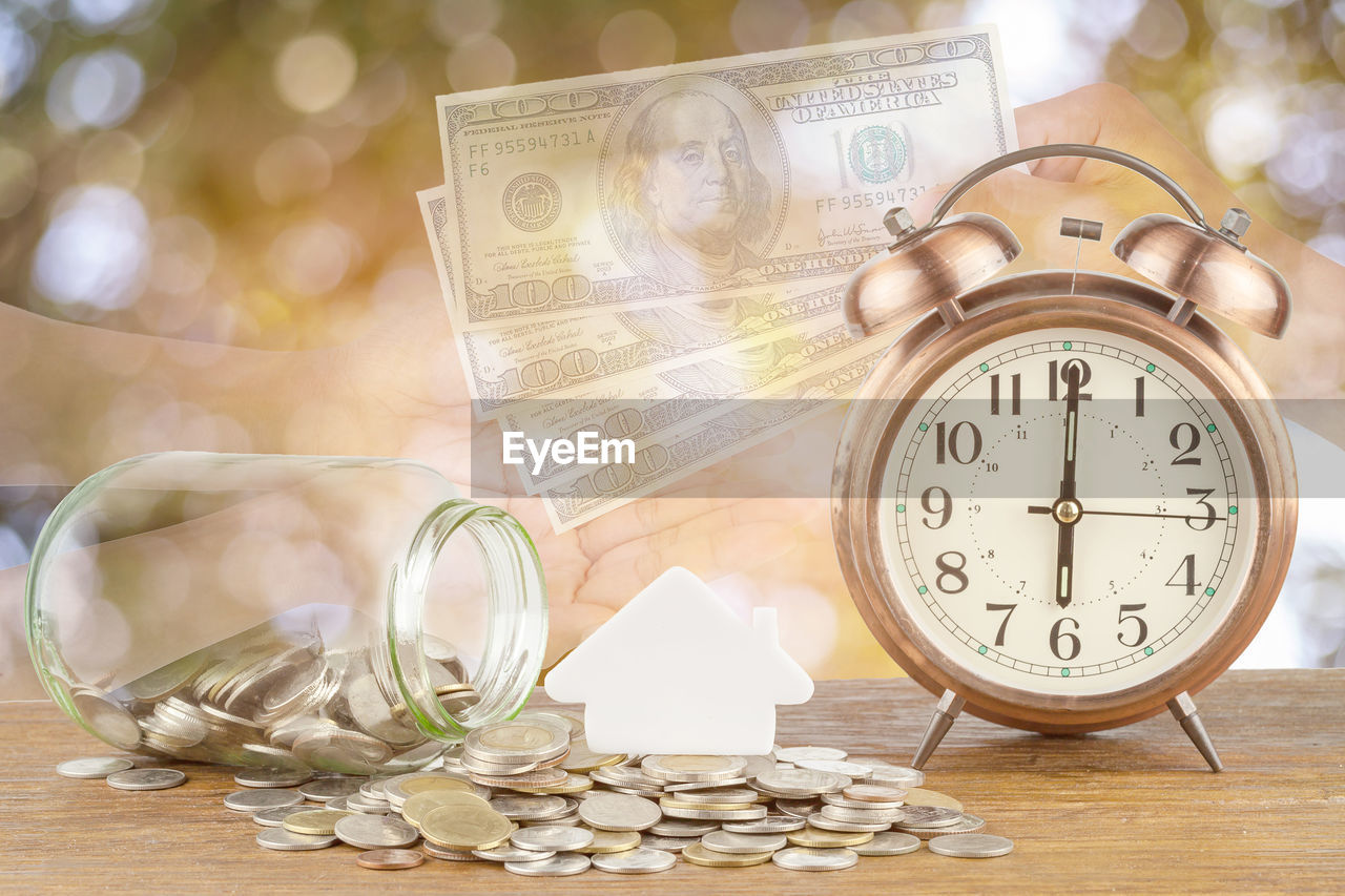 Digital composite image of currency by alarm clock and hands at table