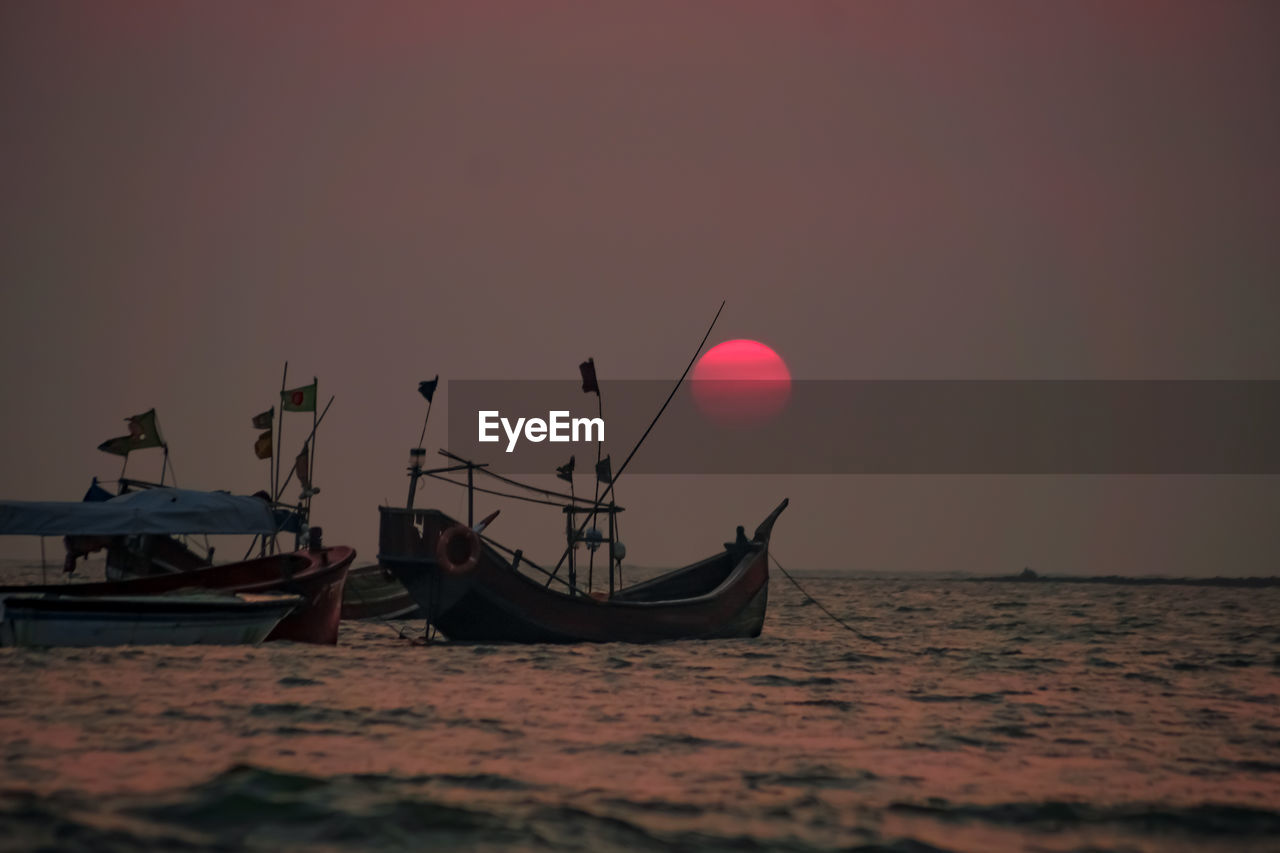 Boat moored in sea against sky during sunset