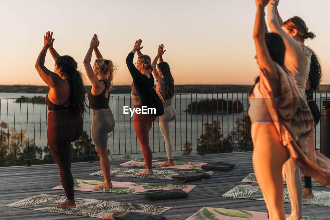 Female friends practicing tree pose together on patio at sunset