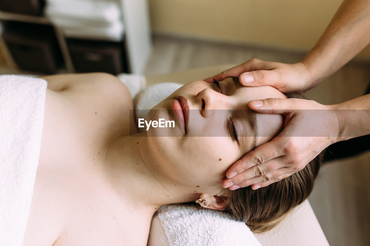 Masseur doing massage on a woman's face at the spa.