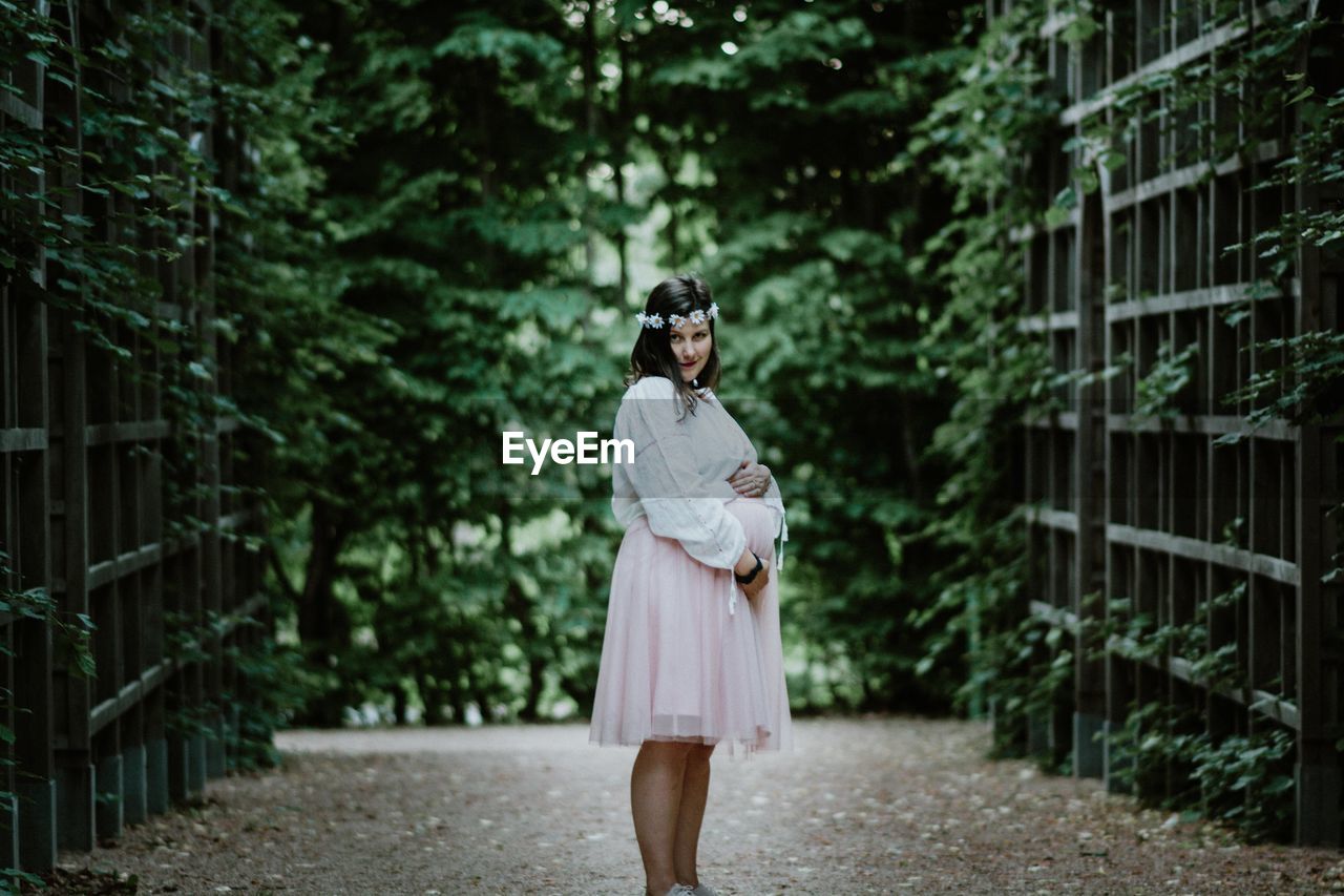 Portrait of pregnant woman standing against trees