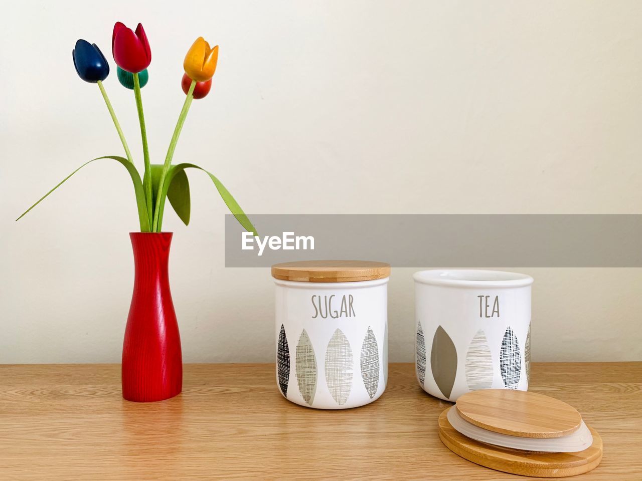 Close-up of tulips in vase on table against wall with tea and sugar jars