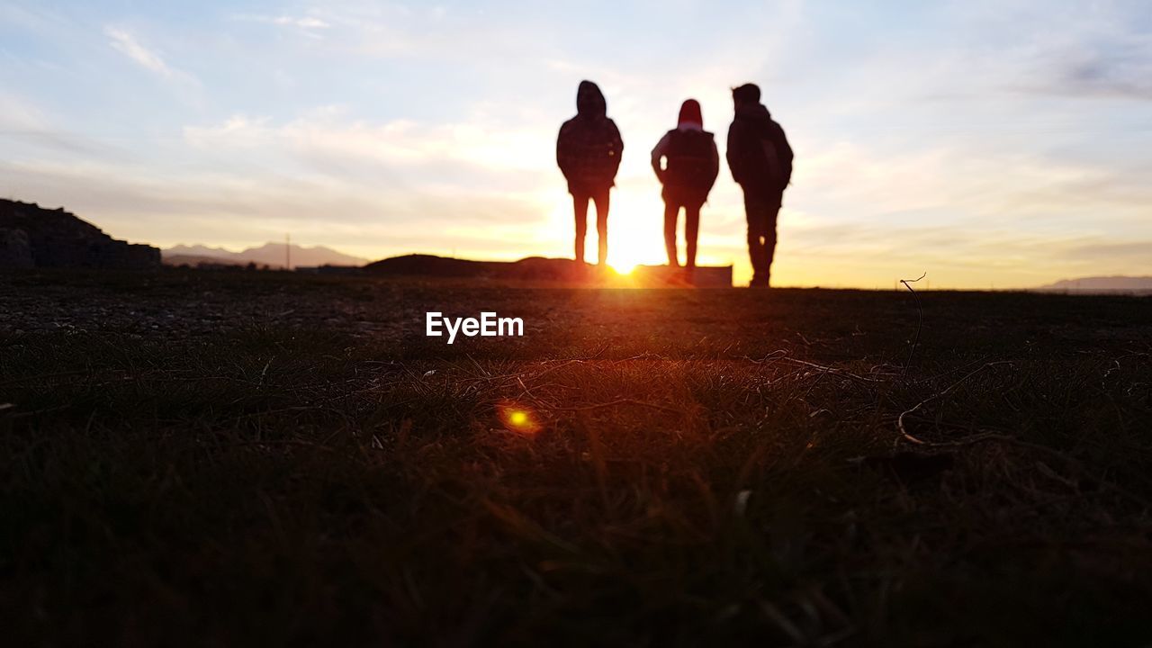 Silhouette family standing on land against sky during sunset