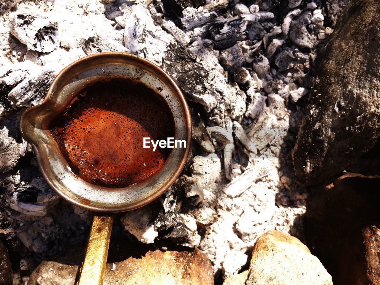Close-up high angle view of tea in container on burnt firewood