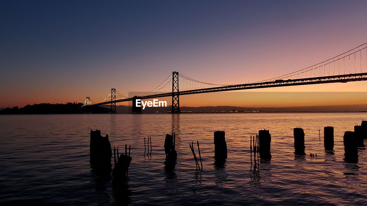 SILHOUETTE OF SUSPENSION BRIDGE OVER SEA AGAINST SKY