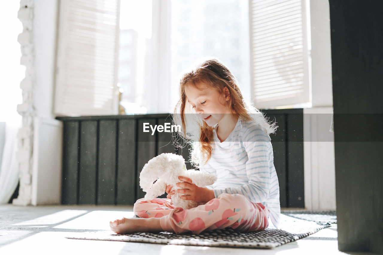 Cute little girl sitting on floor with toy at bright bath room at home