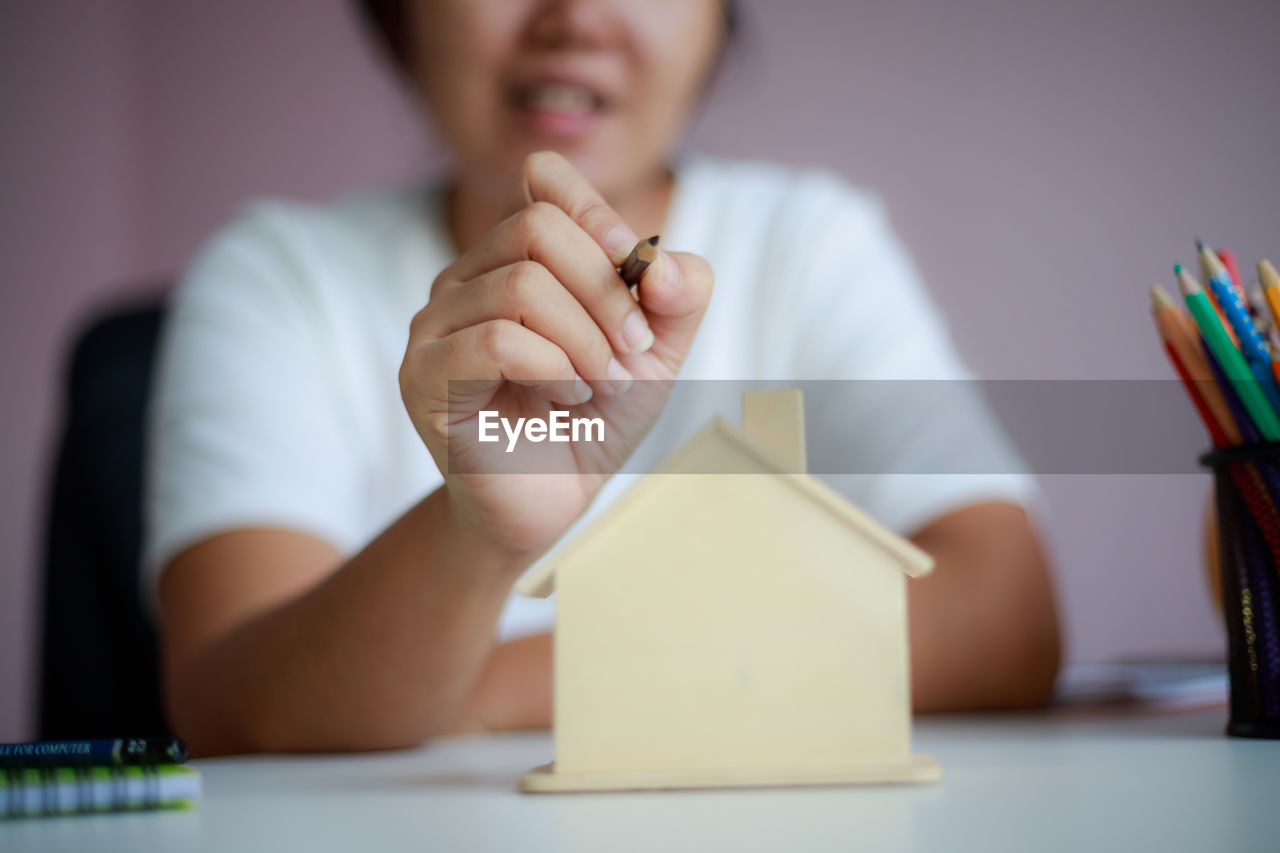 Midsection of woman holding pencil over model home at table