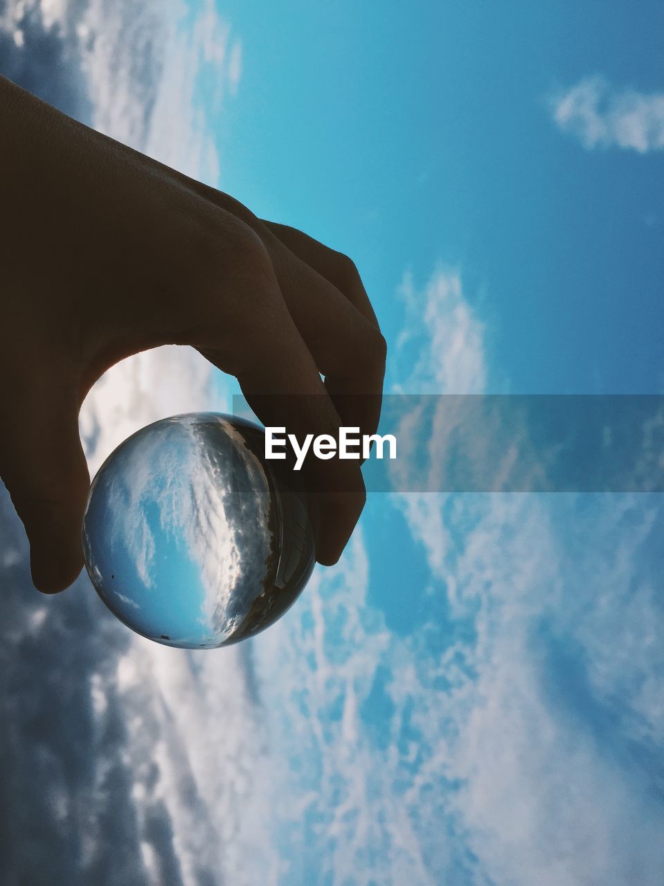 Cropped hand holding crystal ball with sky reflection on it