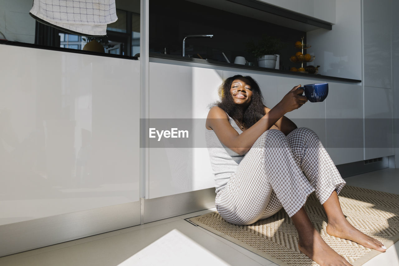 Happy woman sitting with tea cup in kitchen at home