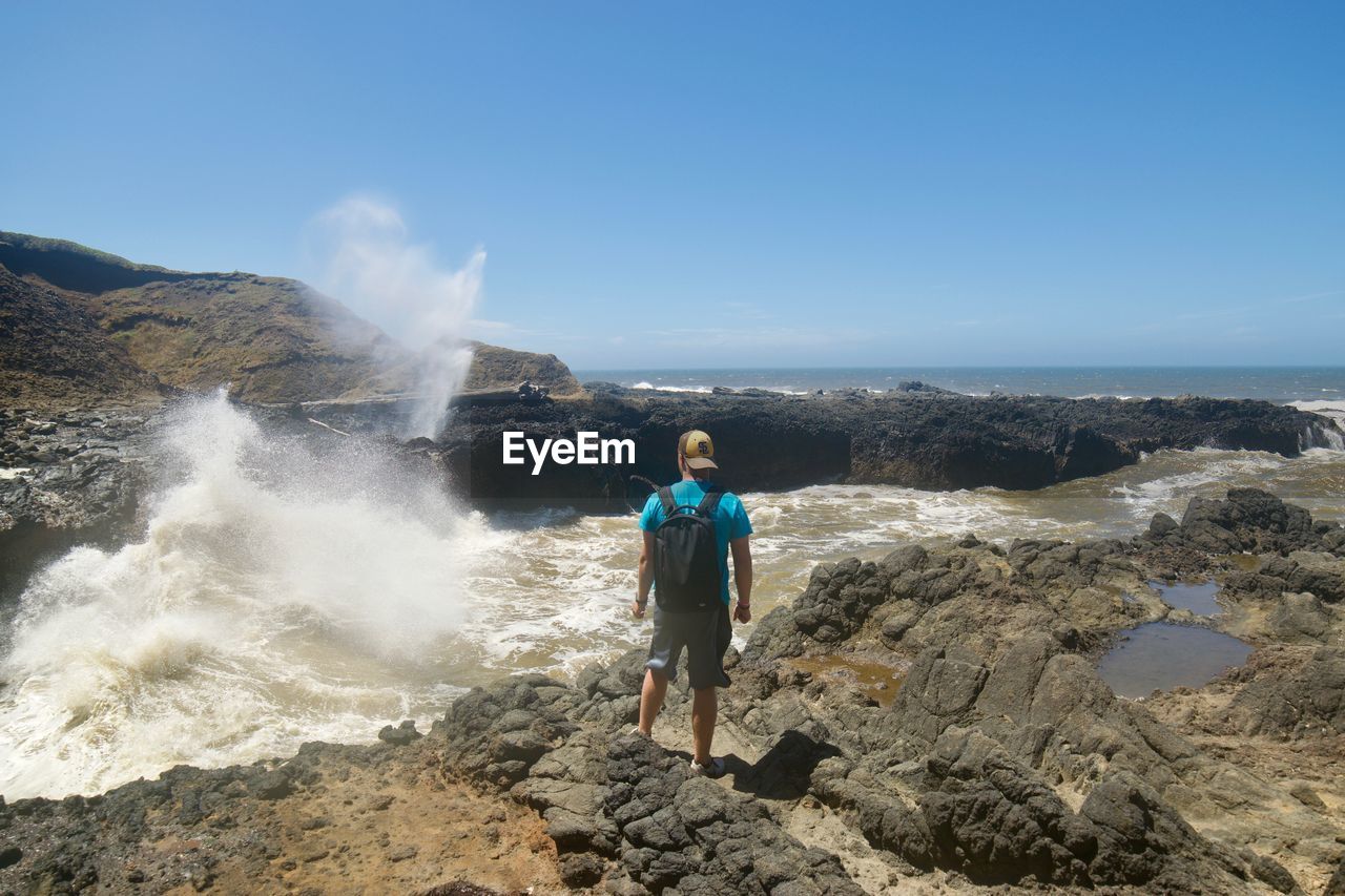 REAR VIEW OF MAN LOOKING AT SEA