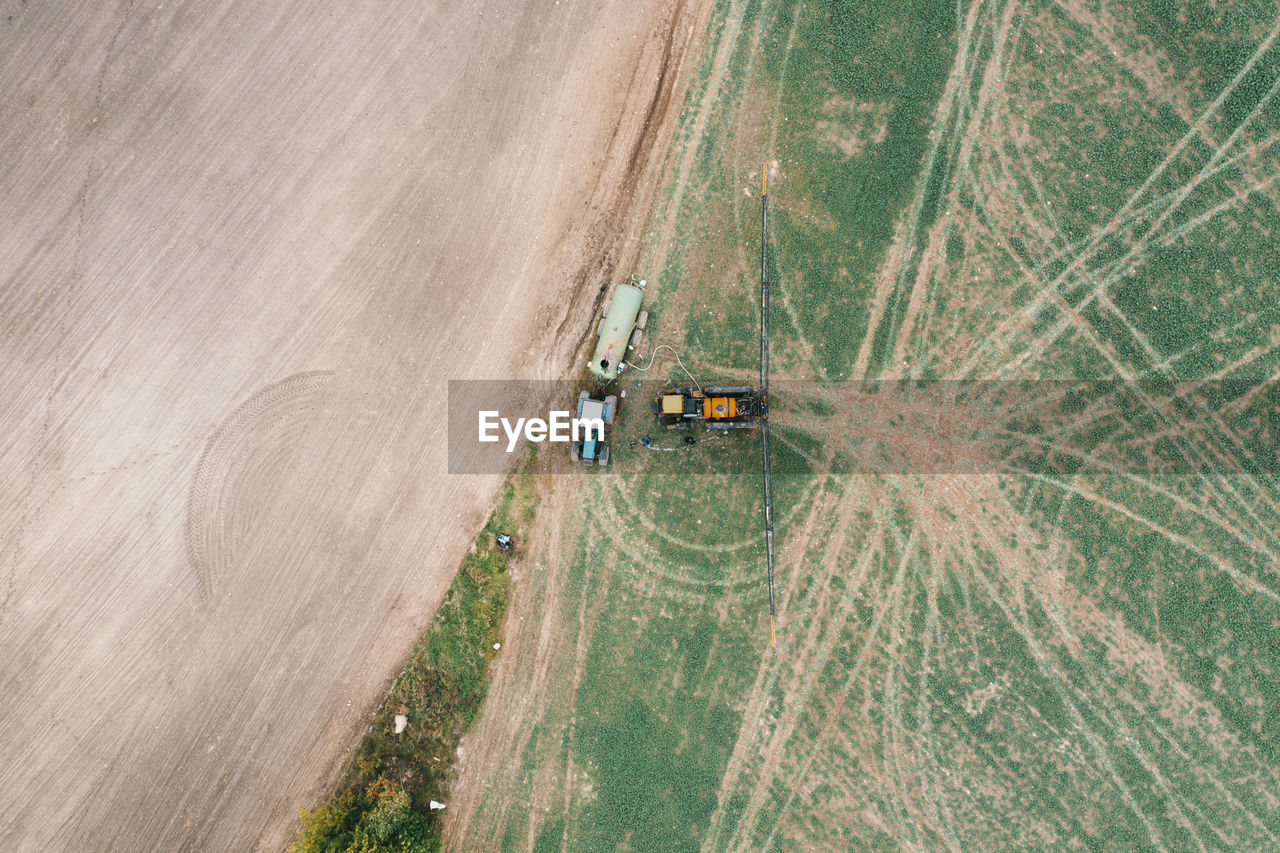 Drone view of a tractor with a sprayer stands near a tractor with a water tank. 
