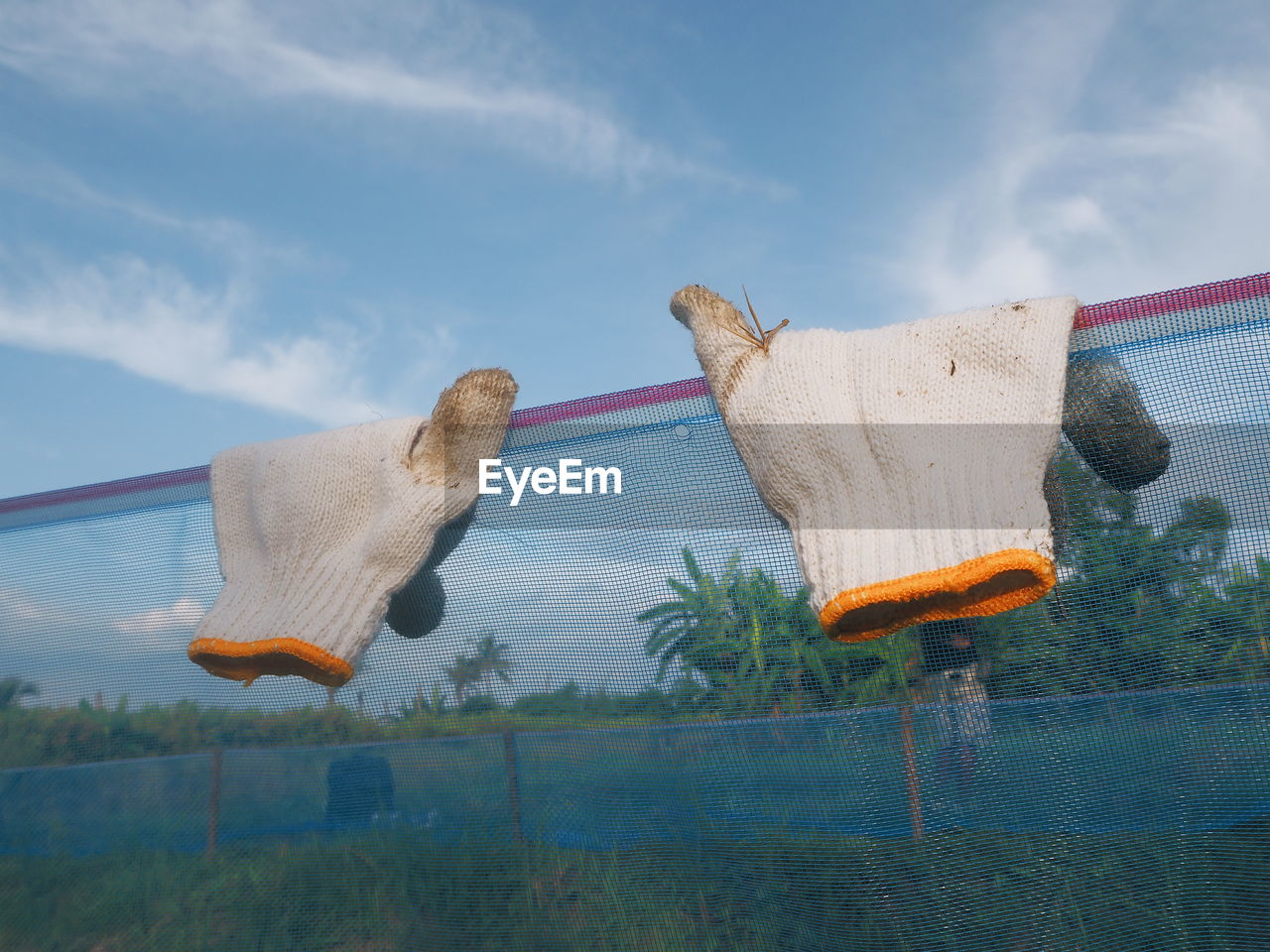 Gloves hanging on fence against sky