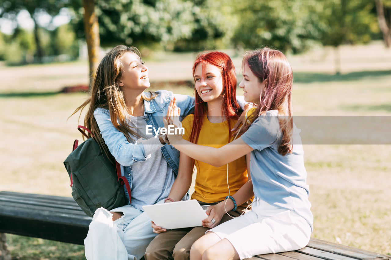 A group of teenage girls sitting and high-fiving with a laptop in the park. meeting on a training
