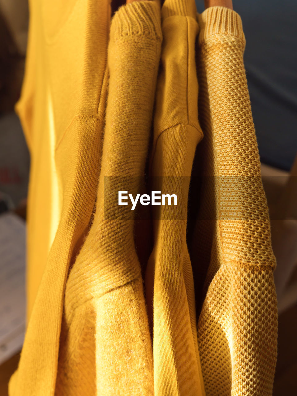 Yellow illuminated color winter sweaters on wooden hangers. trendy fashion autumn cozy clothes.