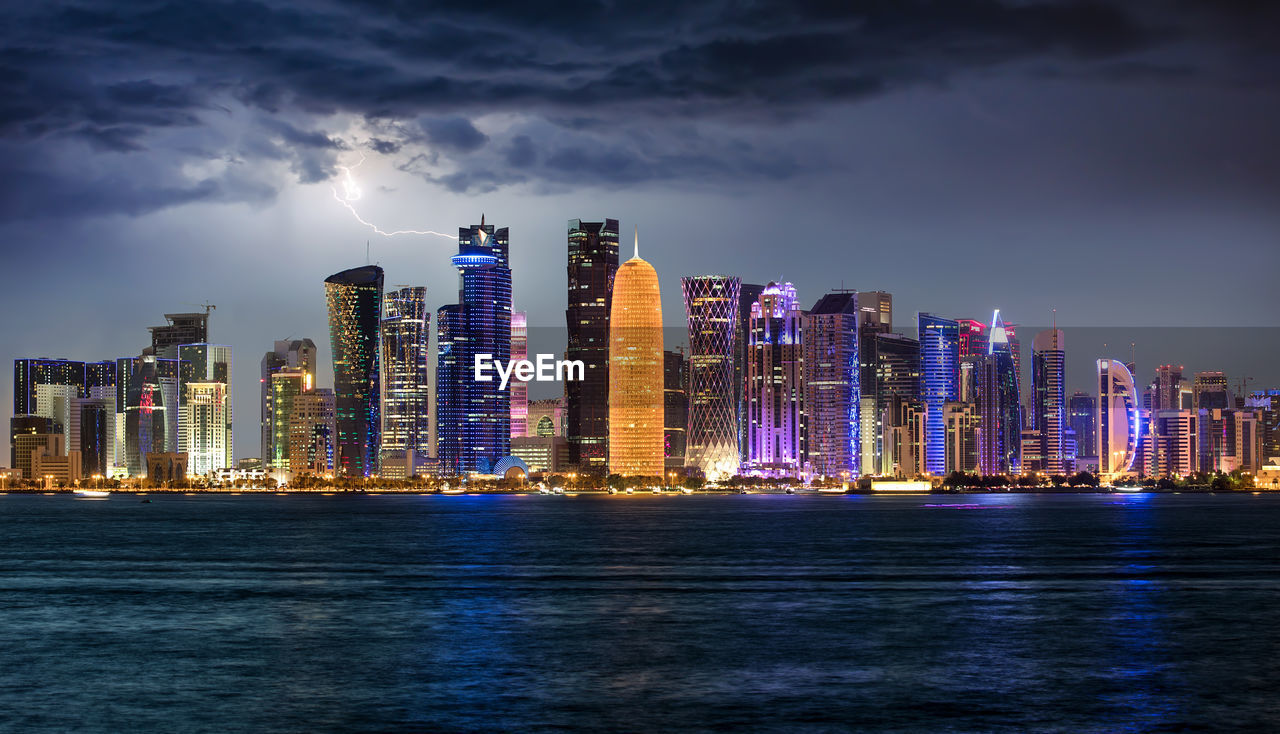 Sea by illuminated buildings against sky at dusk