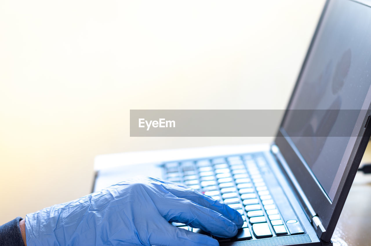 A man in blue gloves work on his laptop from home, corona virus