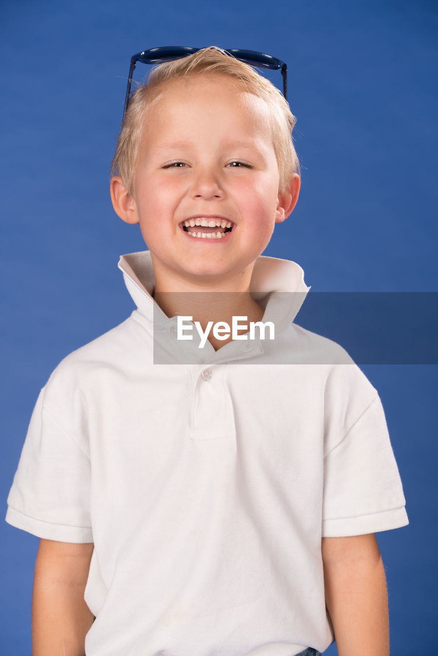 Portrait of cute happy boy standing against blue background