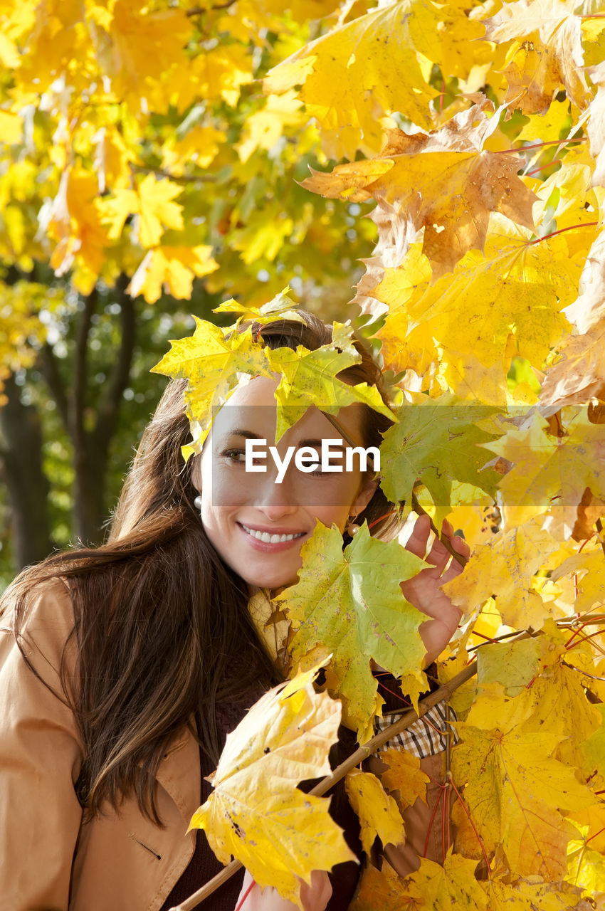 Smiling woman standing by trees in park during autumn