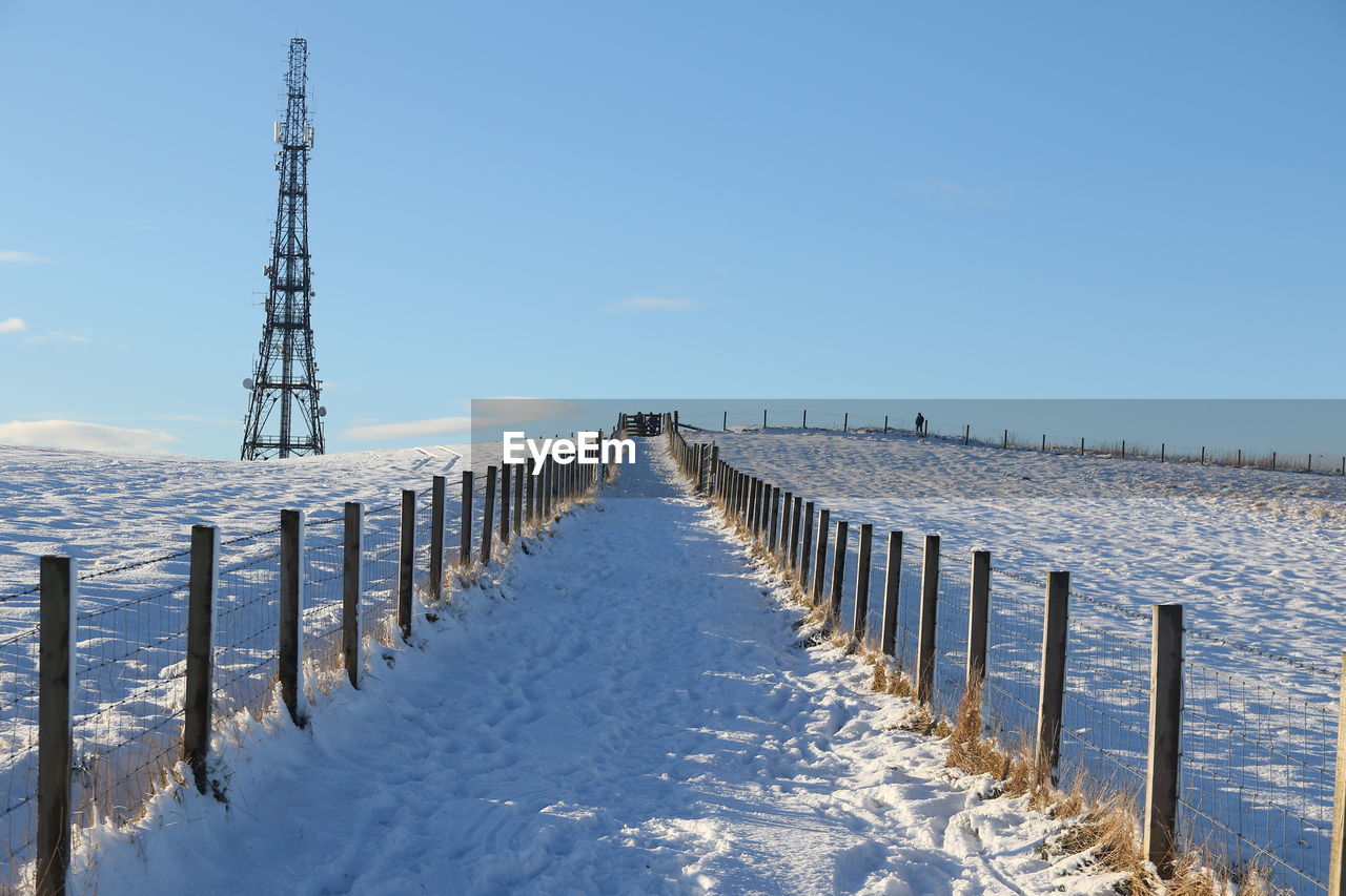 Wooden posts on snow covered field against sky