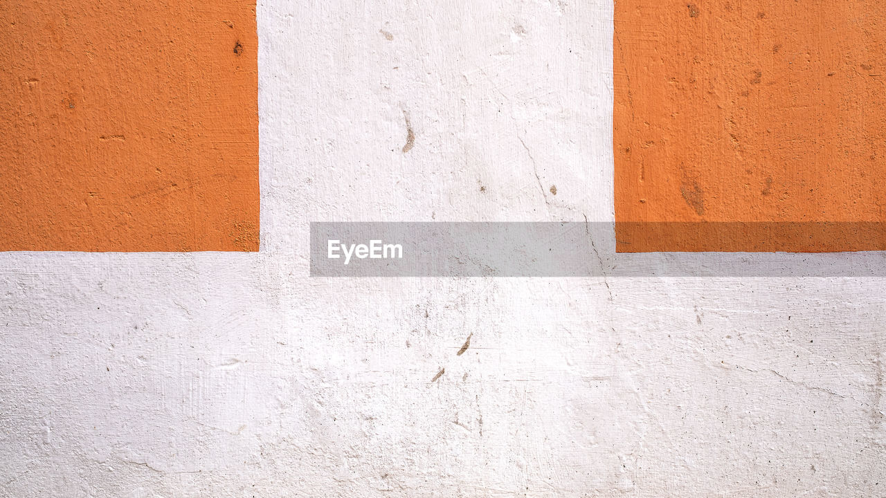 Old cement wall painted orange and white divided into squares for wallpaper and background.