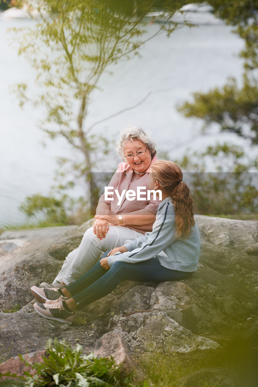 Grandmother and granddaughter talking while sitting on rock in park