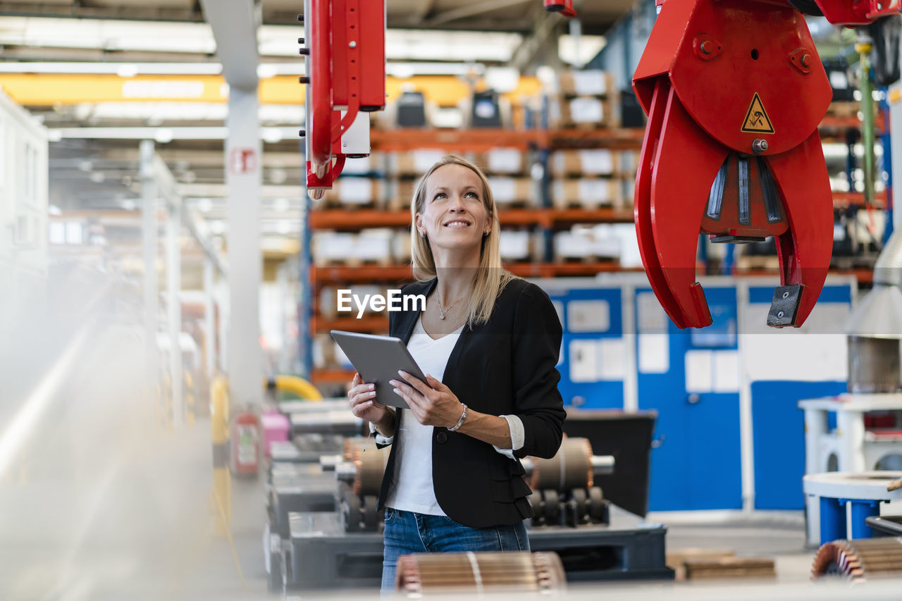 Smiling businesswoman examining claw while holding digital tablet at factory