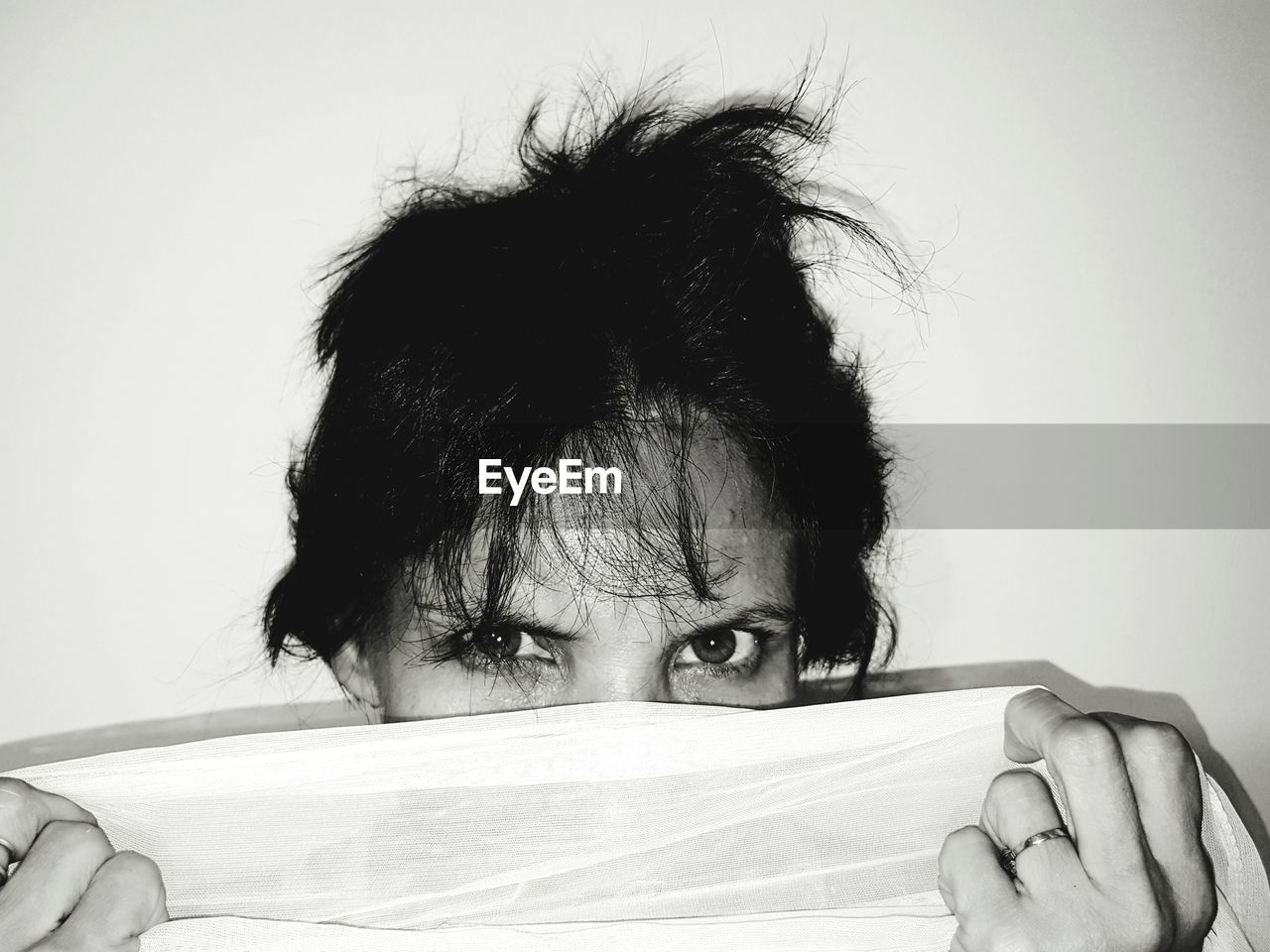 Portrait of woman holding fabric over face against wall