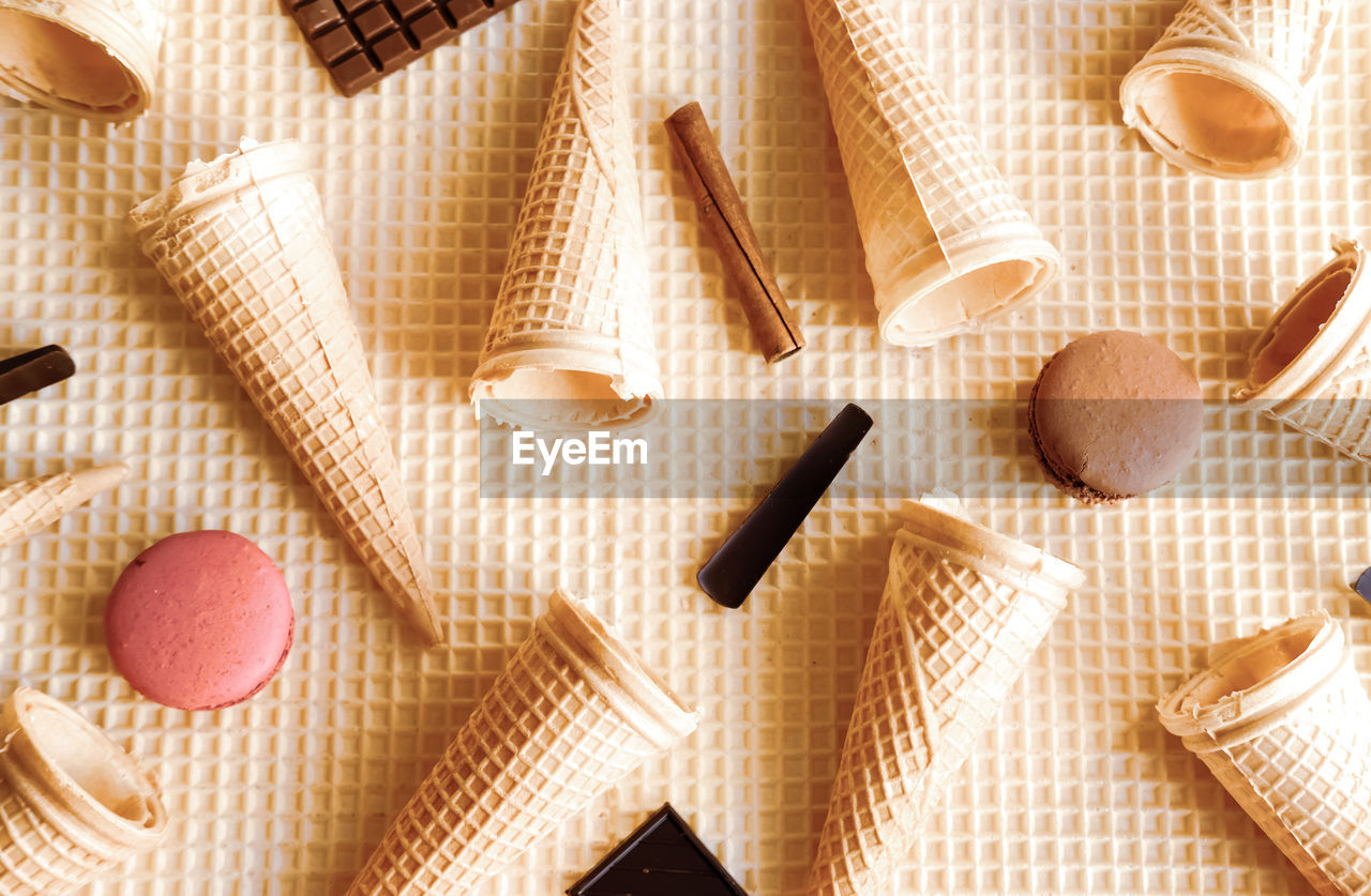 Macarons, chocolates, cinnamon sticks and ice cream cones on waffle background. sweet food concept.