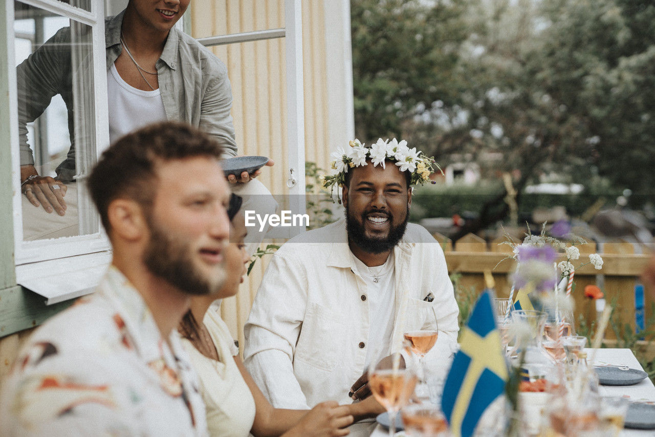 Portrait of happy young man wearing tiara while sitting with friends during dinner party at cafe