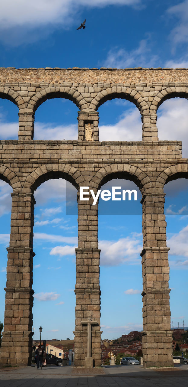 Bird flying with wings open above segovia viaduct with religious symbol, spain