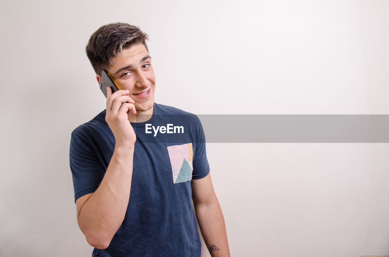 YOUNG MAN USING SMART PHONE AGAINST WALL