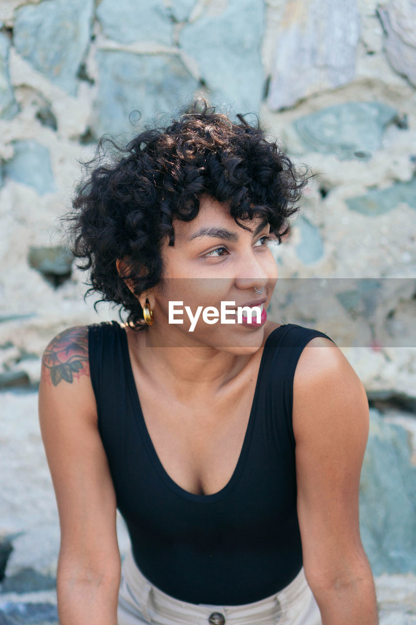 Crop happy young african american female with curly hair and tattoo on shoulder looking away on blurred background