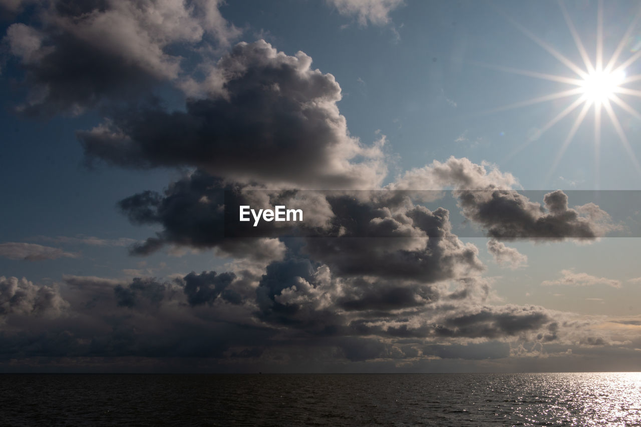 Low angle view of sunlight streaming through clouds over sea