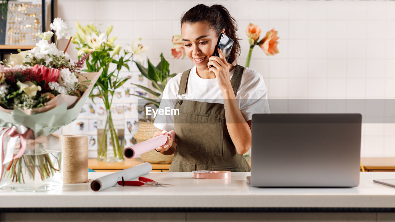 YOUNG WOMAN USING MOBILE PHONE WHILE STANDING ON TABLE AT HOME