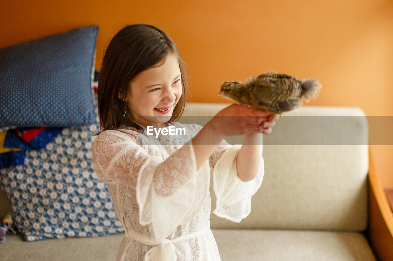 A joyful child holds a baby bird up close to her face to study it