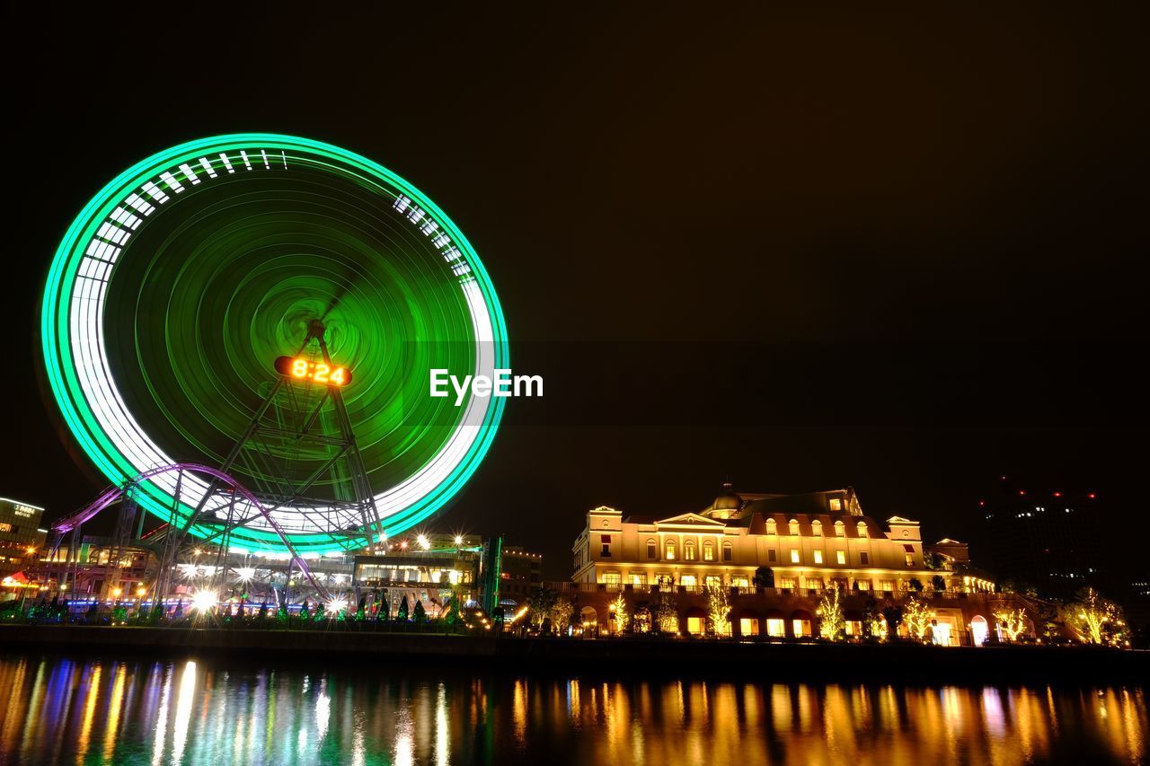 Illuminated ferris wheel digital clock reflected in water