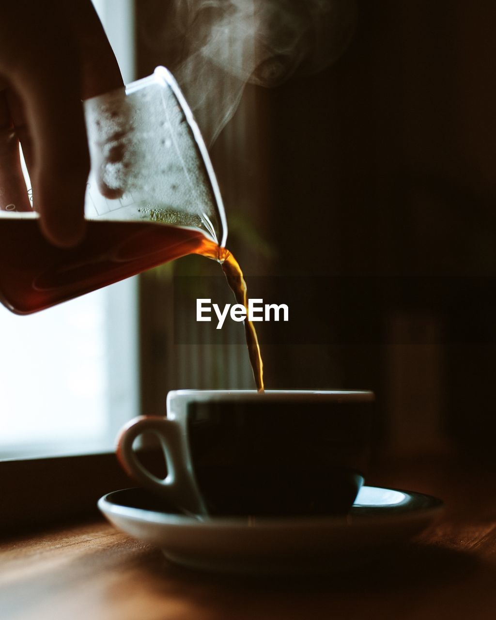 Cropped hand pouring black coffee in cup at home