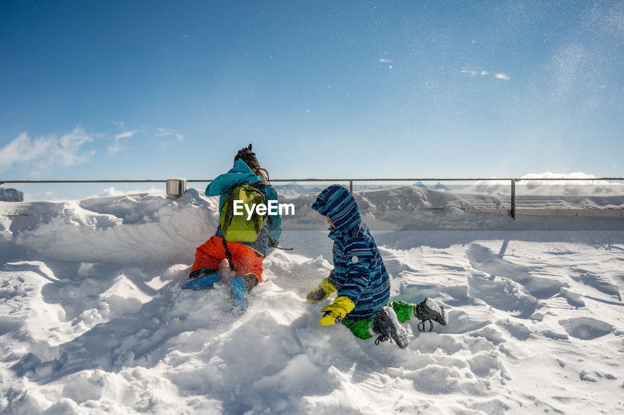 Kids playing in snow covered land during winter against sky