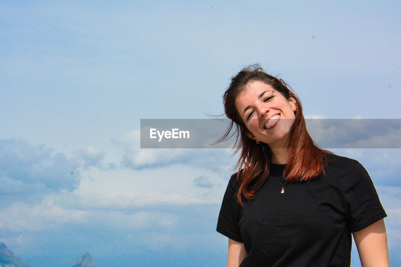 Portrait of smiling woman sticking out tongue against blue sky